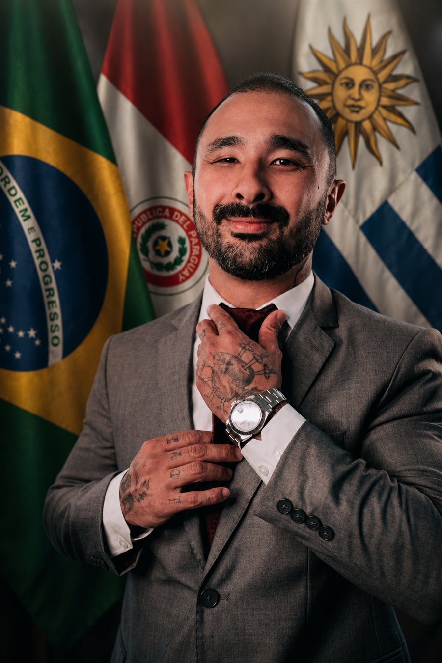 Totti Maikuma diante das bandeiras do Brasil, Paraguai e Uruguai, representando atuação territorial e visão Mercosul